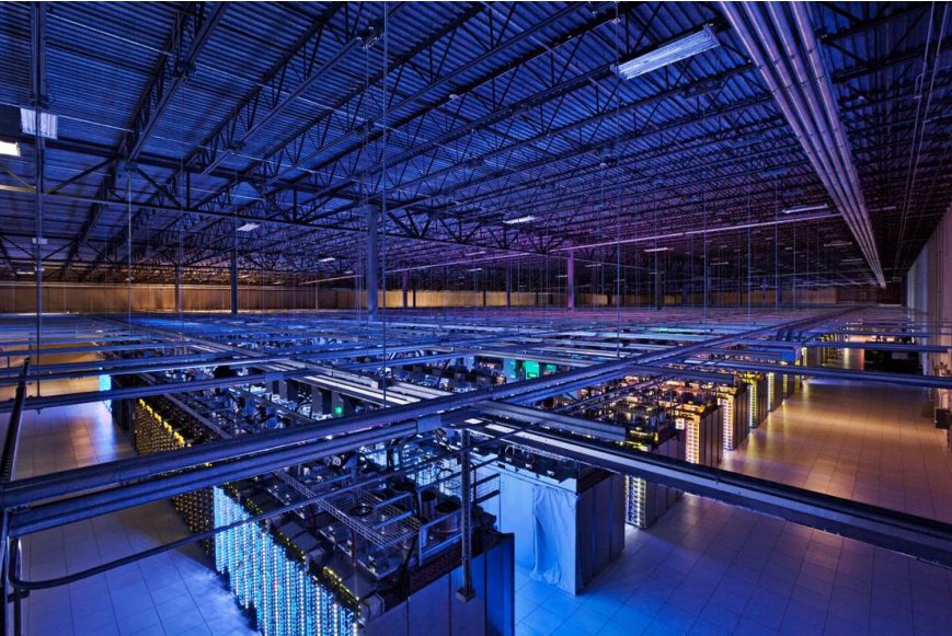 Interior of a large data center hall with long rows of server racks under blue lighting.